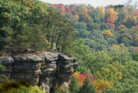 edge of cliff over looking tall forrest. trres are red and orange colors of fall.